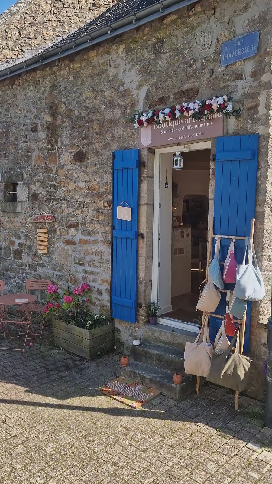 La façade en pierre de l'atelier-boutique, volets bleus, sacs exposés devant la porte